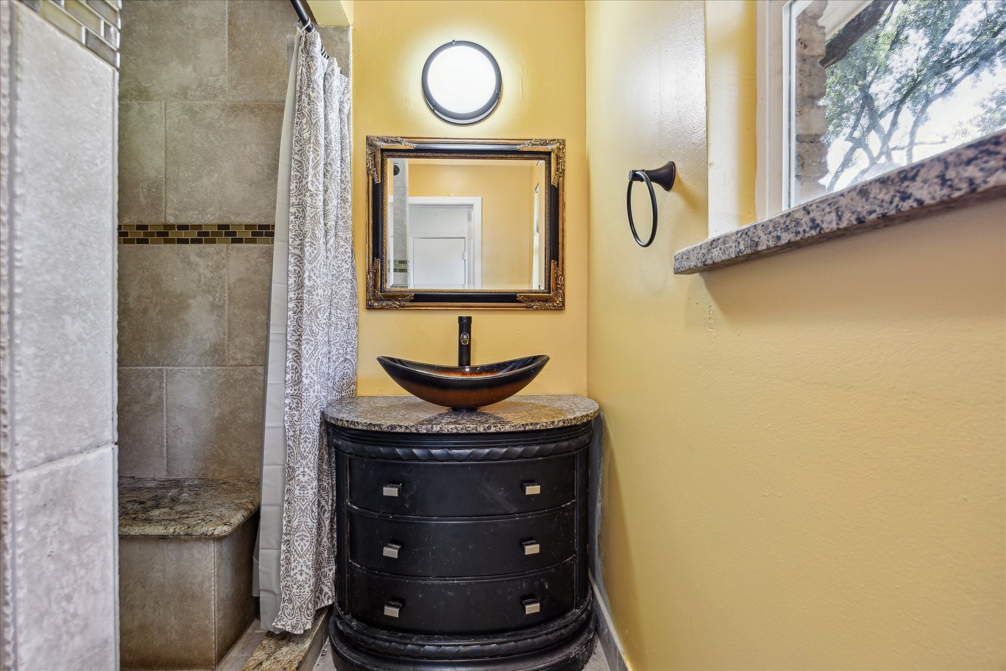 5419 Beechnut Street Houston, TX 77096 - Photo 19 of 28 Updated primary bath with granite vanity, artistic vessel sink, framed mirror, and walk-in shower with tile surround and seating.