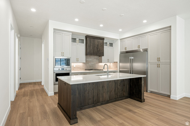 684 West High Tide Place, Unit 131 St. George, UT 84790 - Photo 3 of 27 Modern kitchen featuring a large central island with a light-toned countertop, wood-finish flooring, recessed lighting, stainless steel appliances, and two-tone cabinetry with gold-finish hardware
