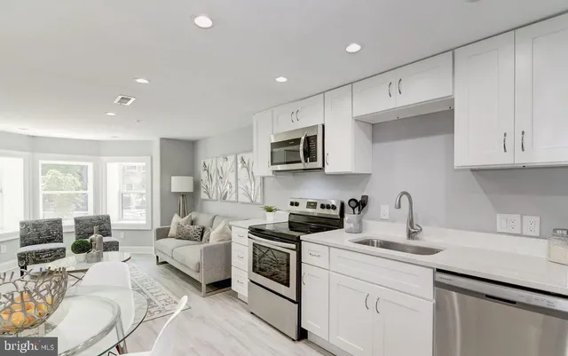 a kitchen with stainless steel appliances granite countertop a sink dishwasher stove and white cabinets with wooden floor