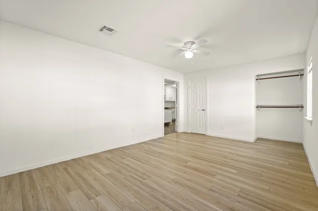a view of an empty room with wooden floor and a ceiling fan