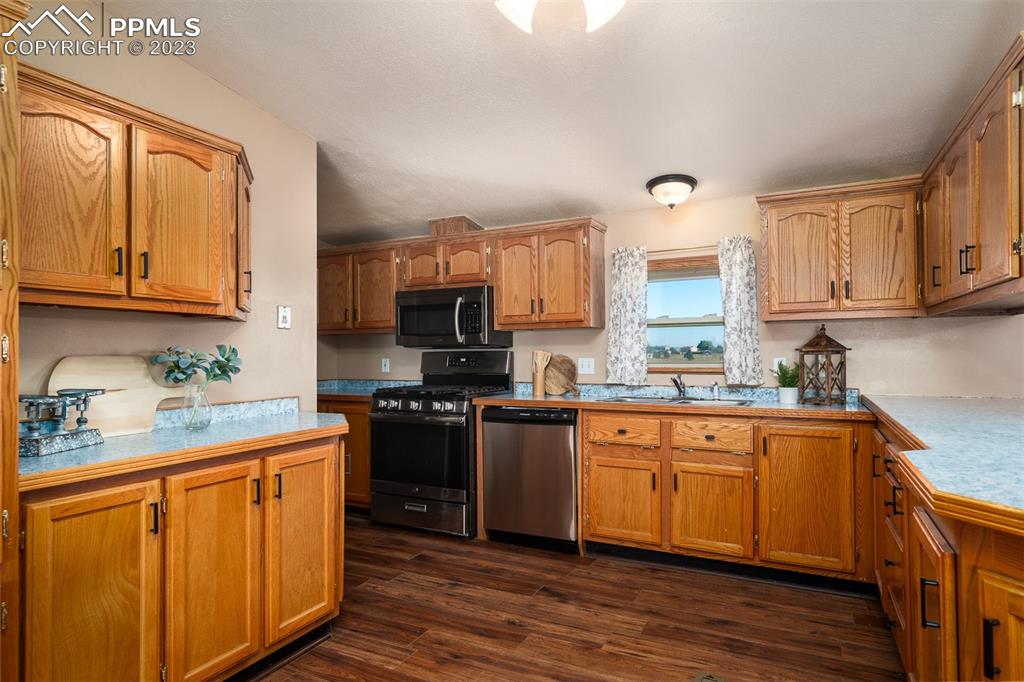 5695 Peerless Farms Road Peyton, CO 80831 - Photo 17 of 50 a kitchen with stainless steel appliances granite countertop a stove top oven a sink dishwasher and a refrigerator with wooden cabinets