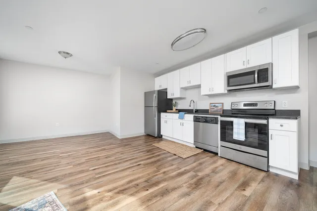 a kitchen with stainless steel appliances a stove top oven a refrigerator white cabinets and wooden floor