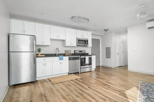 a kitchen with granite countertop a refrigerator a stove a sink and white cabinets with wooden floor