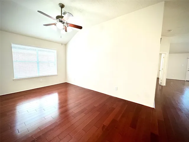an empty room with wooden floor chandelier fan and windows