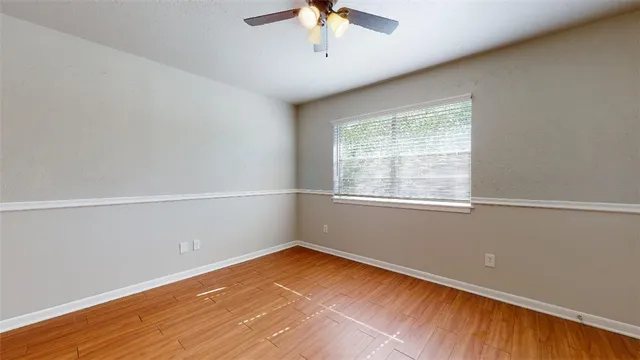 an empty room with wooden floor fan and windows