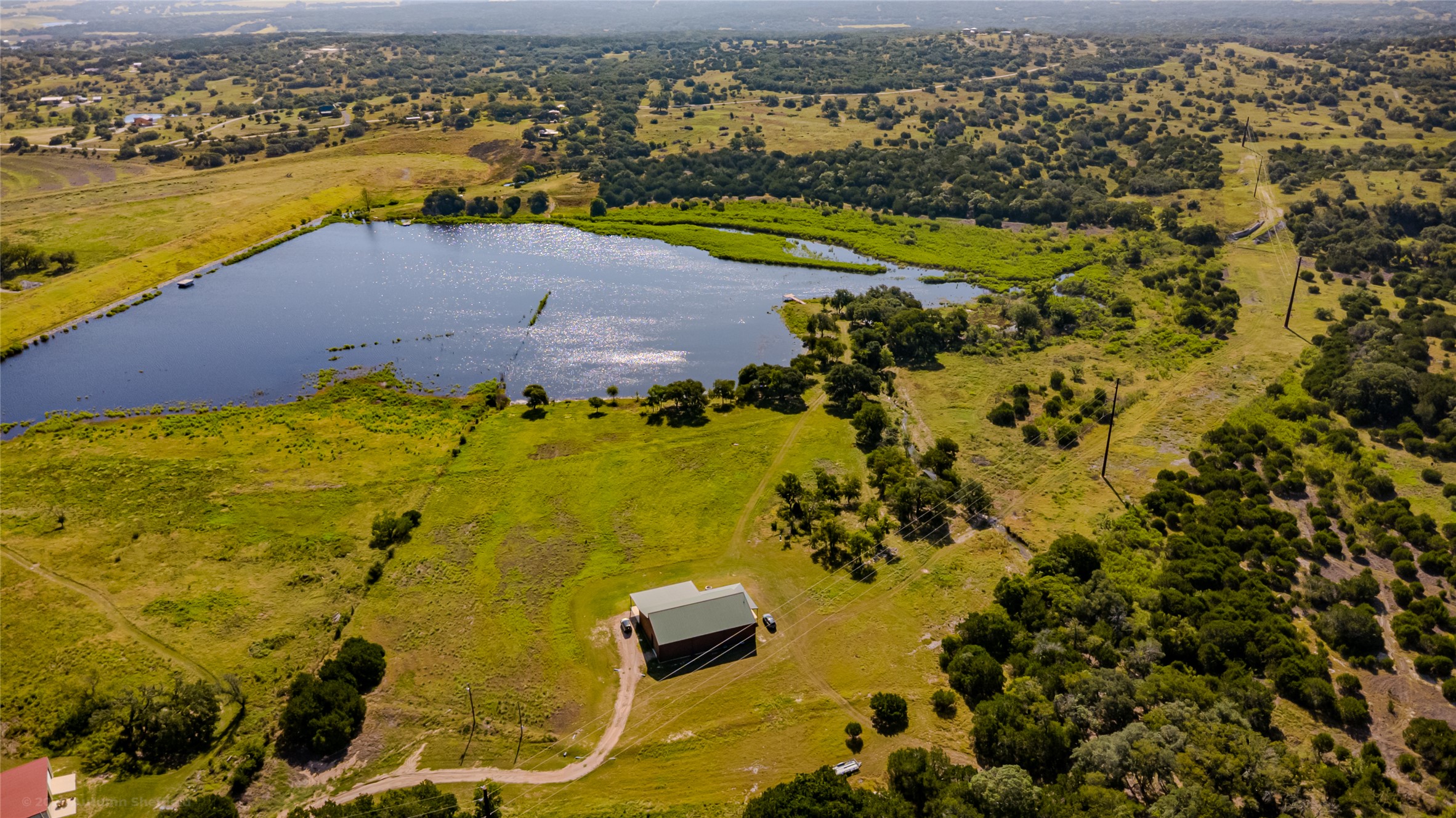 3259 Schumann Road Stonewall, TX 78671 - Photo 8 of 36 Rolling green hills surround a private body of water under open skies.