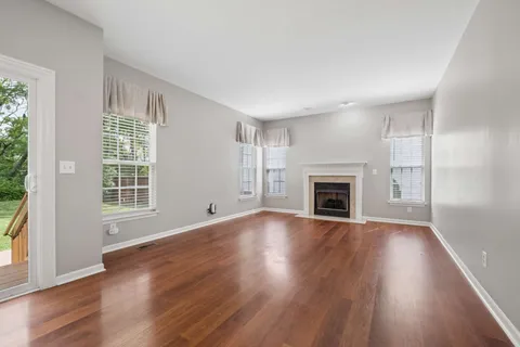 an empty room with wooden floor fireplace and windows