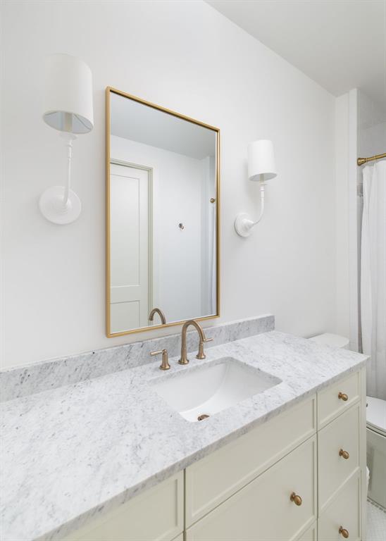 3963 Rochelle Drive Dallas, TX 75220 - Photo 32 of 40 White vanity with integrated sink, stone countertop, gold-framed mirror, and brass-finish fixtures