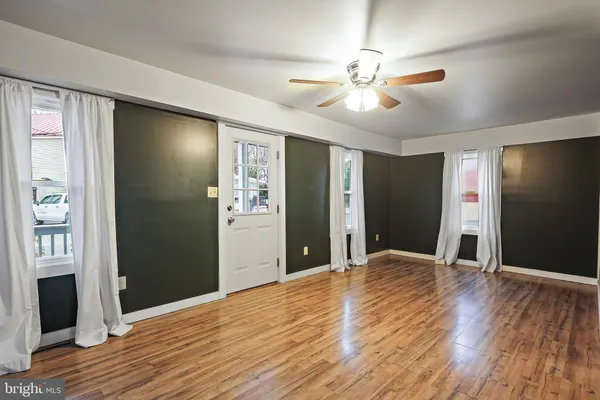 a view of an empty room with wooden floor and a ceiling fan