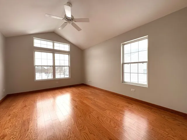 an empty room with wooden floor chandelier fan and windows