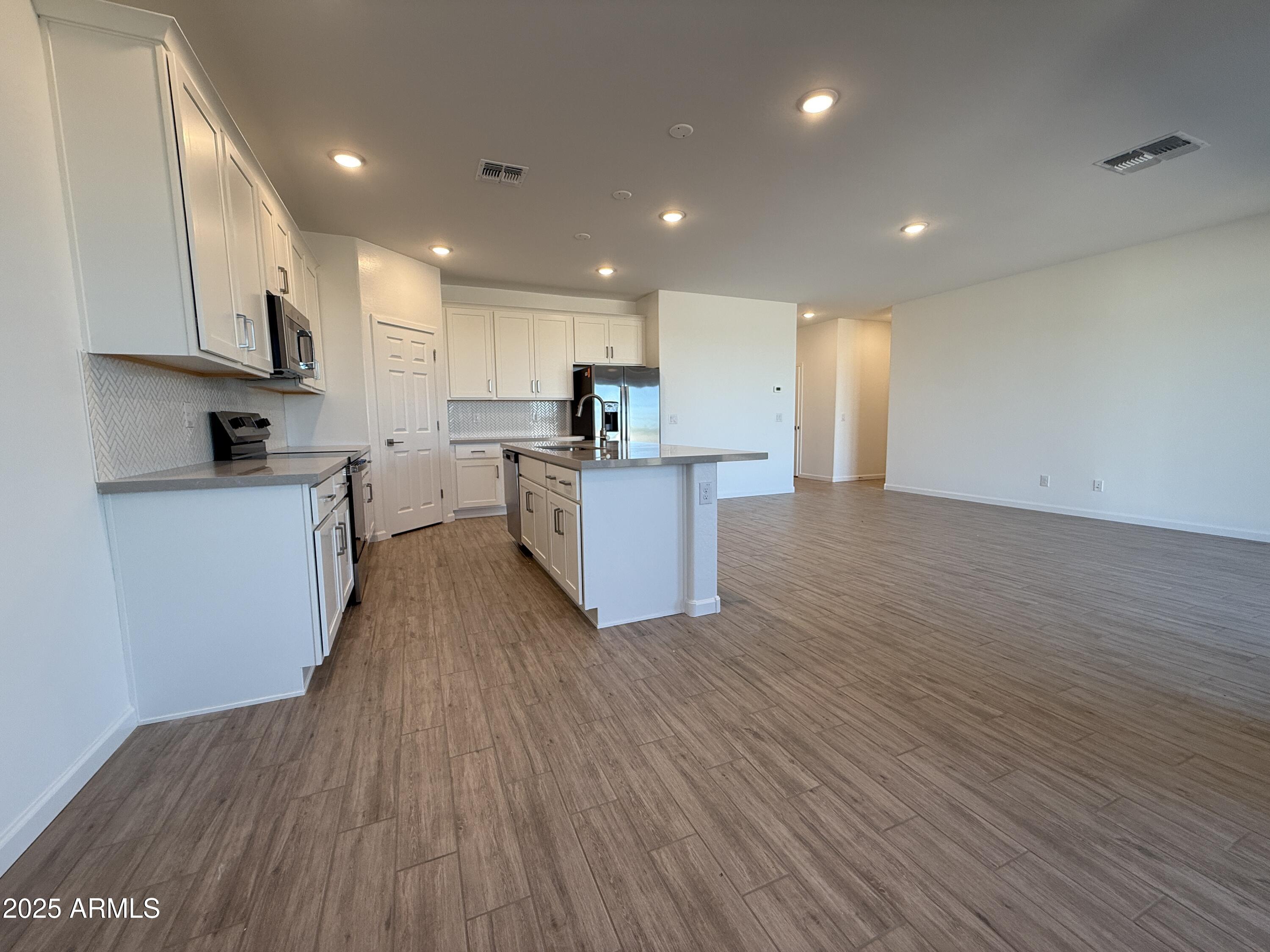 9628 West Tamarisk Avenue Tolleson, AZ 85353 - Photo 19 of 37 a kitchen with stainless steel appliances wooden floors stove and white cabinets