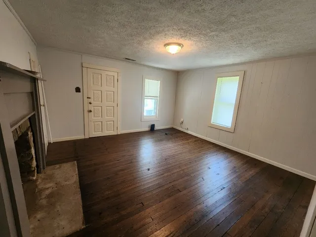 a view of an empty room with wooden floor and a fireplace