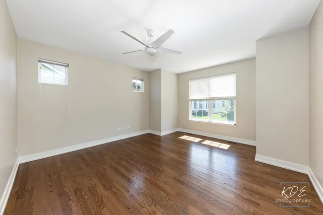 an empty room with wooden floor chandelier fan and windows