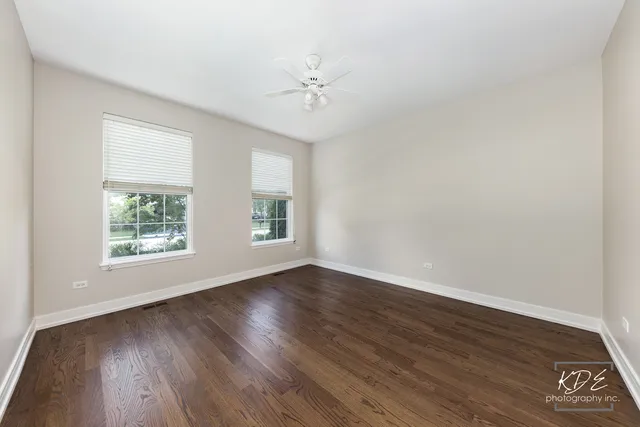 an empty room with wooden floor windows and fan