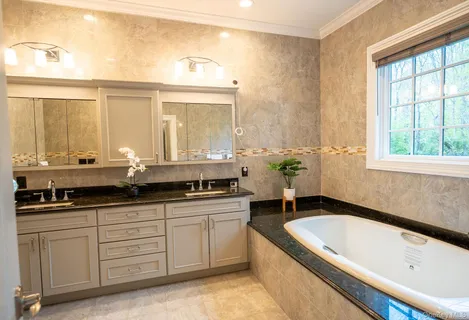 a bathroom with a granite countertop tub a double vanity sink a window and a mirror