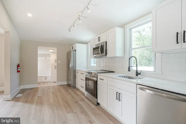 a kitchen with a sink dishwasher a stove and white cabinets with wooden floor