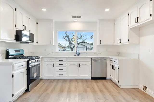 a kitchen with cabinets stainless steel appliances a sink and wooden floor