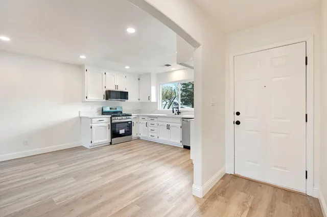 a view of kitchen with granite countertop a stove top oven a sink and white cabinets with wooden floor