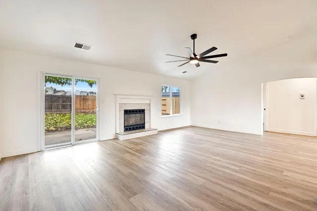 a view of a livingroom with a fireplace a ceiling fan and wooden floor