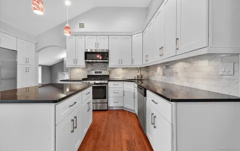 a kitchen with granite countertop a sink and dishwasher a stove top oven with white cabinets