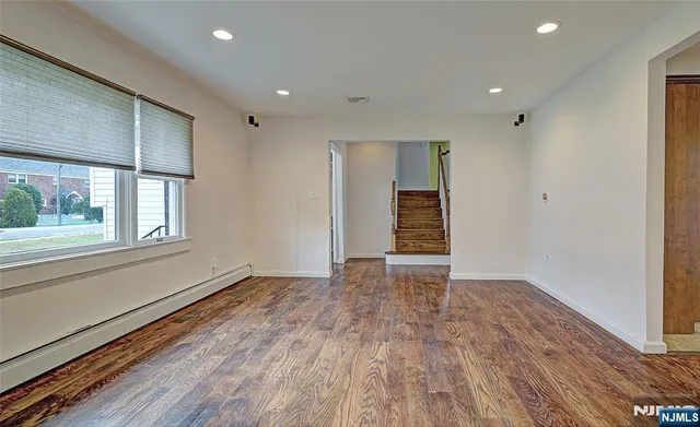a view of an empty room with wooden floor and a window