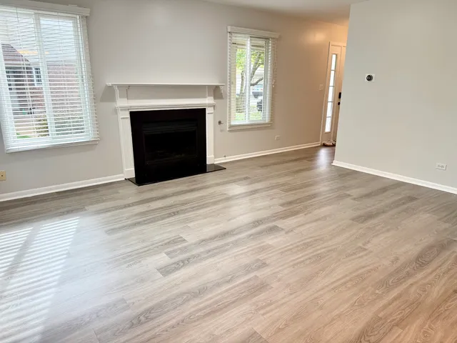 an empty room with wooden floor fireplace and windows