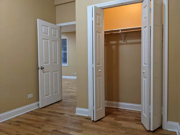 an empty room with wooden floor closet and windows