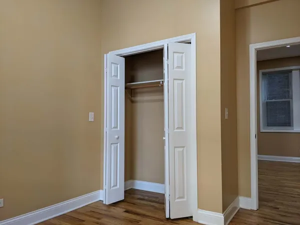 a view of an empty room with wooden floor and closet