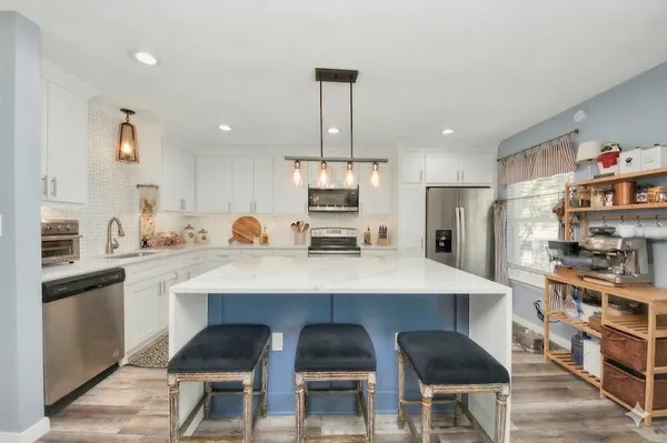 a kitchen with stainless steel appliances kitchen island granite countertop a refrigerator a stove a sink dishwasher and white cabinets with wooden floor