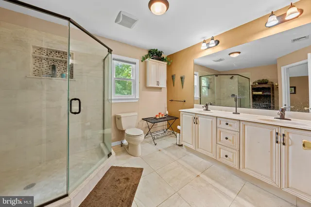 a spacious bathroom with a double vanity sink a toilet a mirror and shower