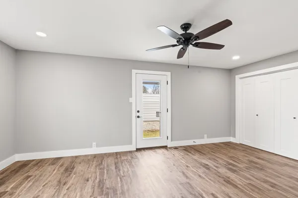 a view of an empty room with wooden floor and a ceiling fan