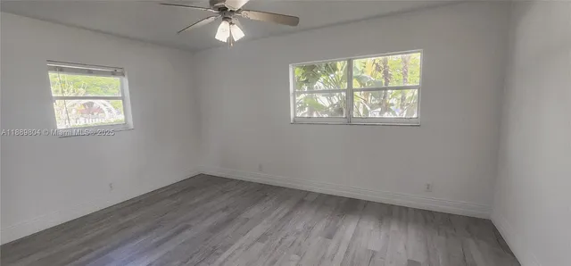 an empty room with wooden floor chandelier fan and windows