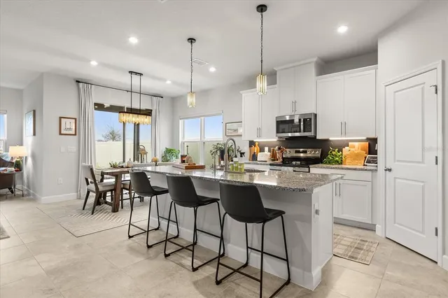 a kitchen with stainless steel appliances kitchen island granite countertop a table chairs sink and cabinets