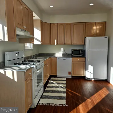 a kitchen with granite countertop a refrigerator a sink dishwasher a stove and a microwave oven on wooden floor