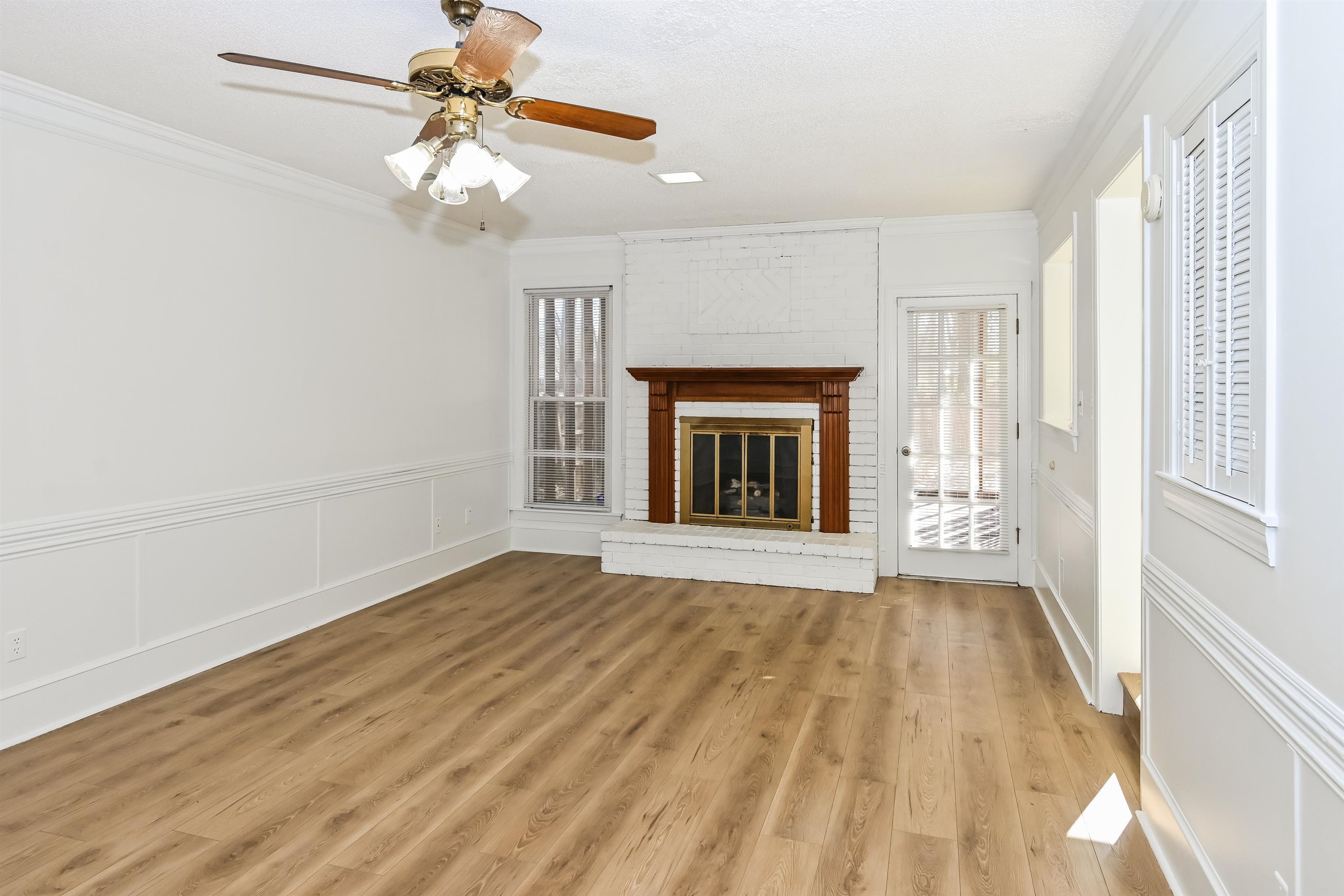 3656 Beaver Run Drive Collierville, TN 38017 - Photo 2 of 18 Unfurnished living room with crown molding, a brick fireplace, ceiling fan, light wood-style floors, and a decorative wall
