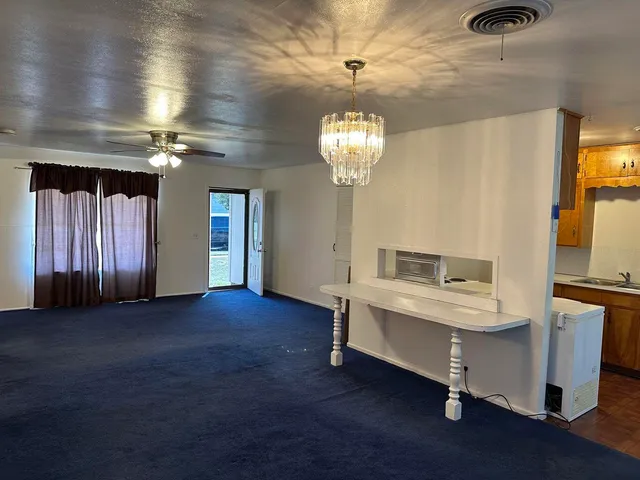 a view of a livingroom with a furniture chandelier fan and kitchen view