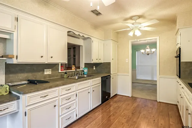 a kitchen with a sink dishwasher a stove and white cabinets with wooden floor