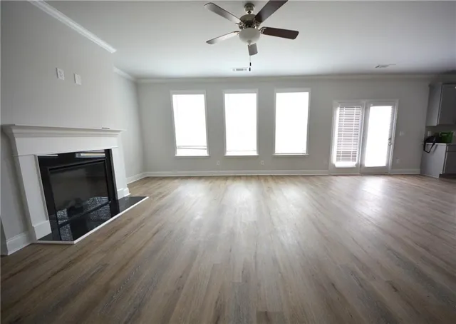 an empty room with wooden floor ceiling fan and windows