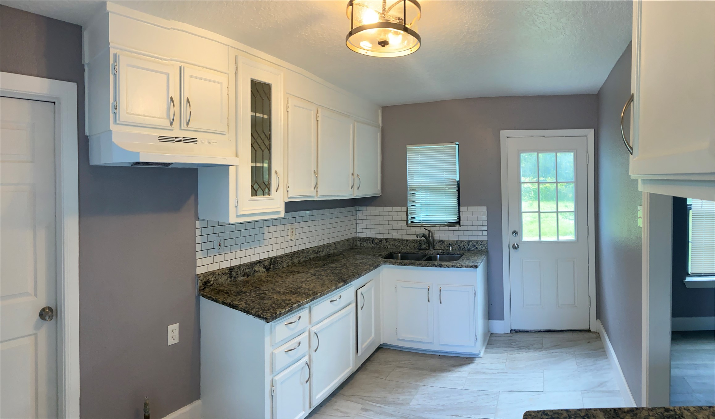 7547 Laura Koppe Road Houston, TX 77028 - Photo 7 of 11 This kitchen features white cabinetry, granite countertops, and a classic subway tile backsplash. It has a window for natural light and a door leading outside, creating a bright and functional space.