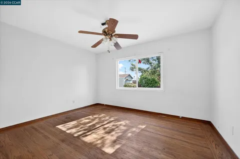 an empty room with wooden floor ceiling fan and window