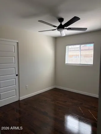 a view of an empty room with wooden floor and a ceiling fan