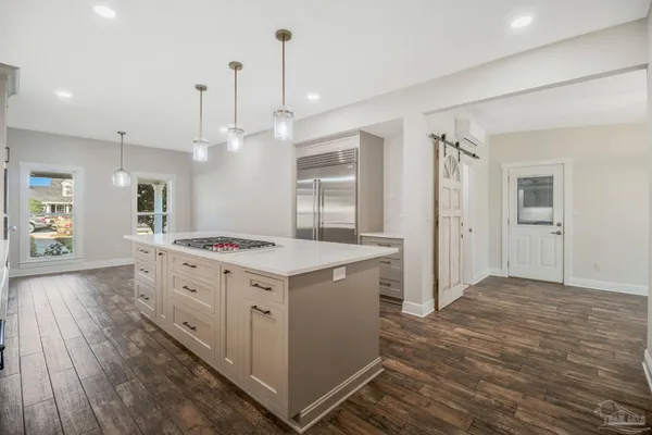 a large kitchen with stainless steel appliances a sink dishwasher a refrigerator and white cabinets with wooden floor