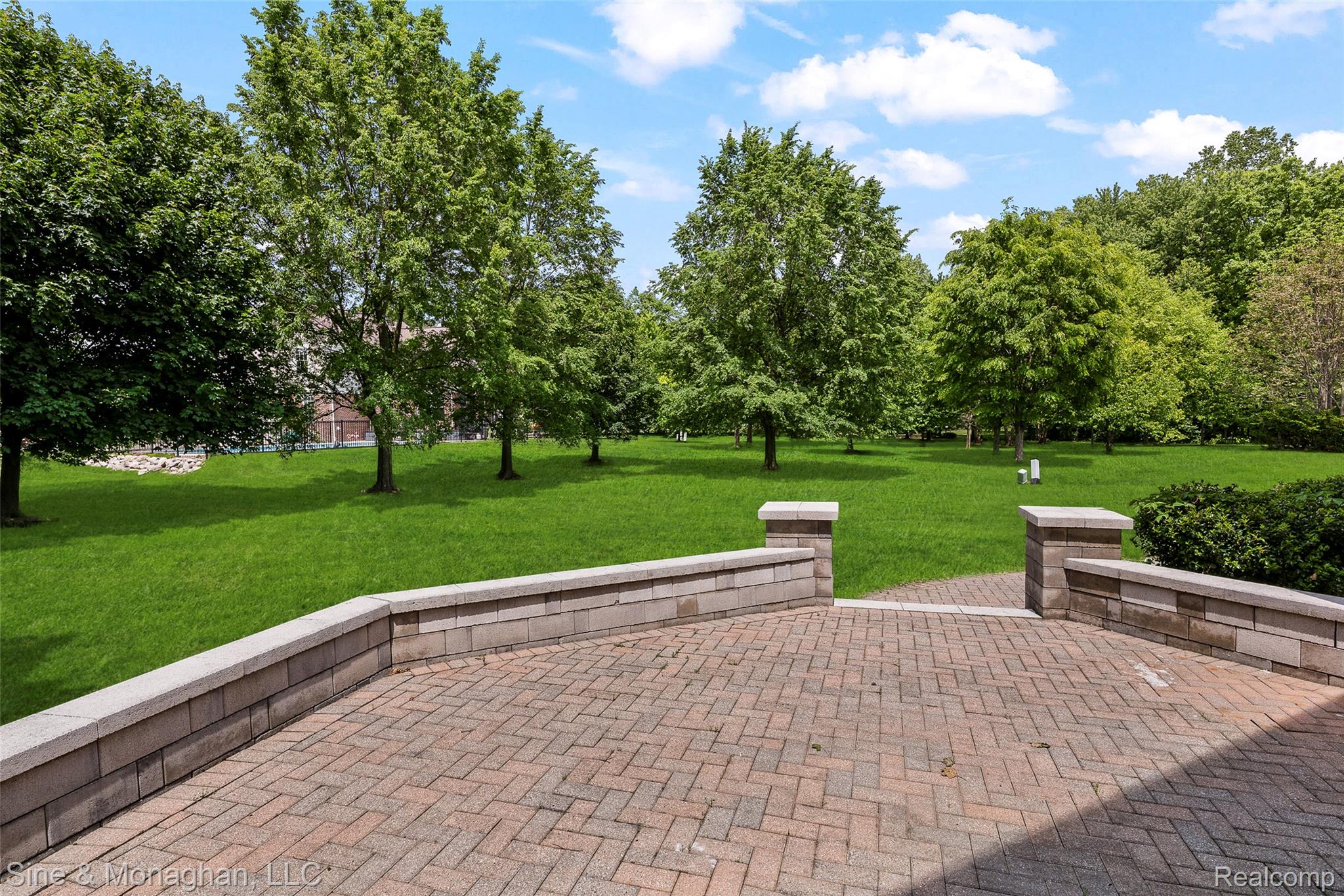 48322 Antique Road Canton, MI 48187 - Photo 37 of 45 Expansive paver patio featuring a low stone wall, stone pillars, and green lawn with mature trees