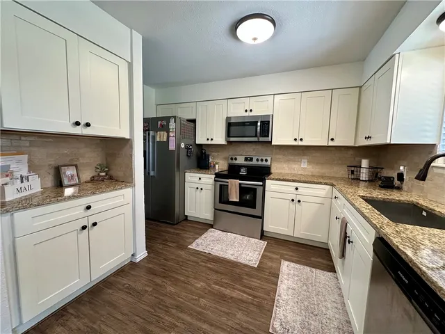 a kitchen with granite countertop a sink cabinets stainless steel appliances and a window