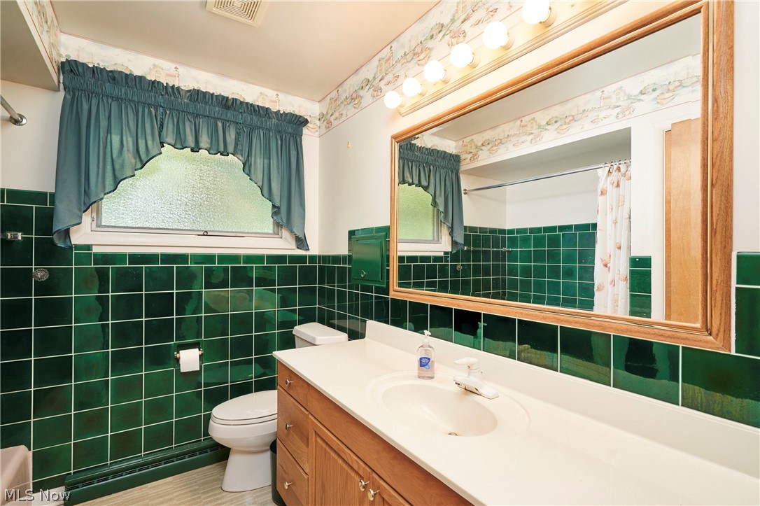 299 West Caston Road New Franklin, OH 44319 - Photo 14 of 23 Bathroom featuring green tile wainscoting, a wood-finish vanity with a white countertop, and a large framed mirror with overhead lighting
