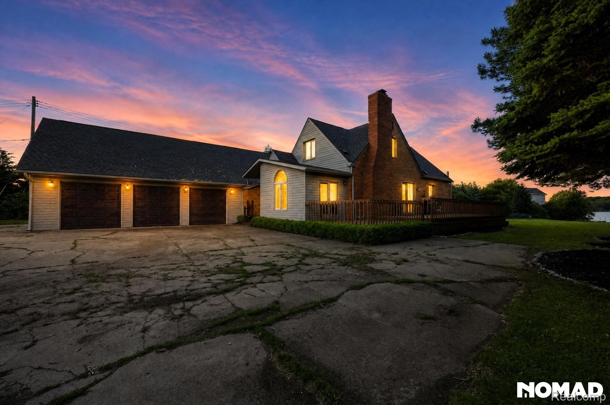 8315 Hilton Road Brighton, MI 48114 - Photo 25 of 26 Brick and siding exterior featuring a three-car garage with individual doors, a multi-level wood deck, a prominent brick chimney, and a landscaped lawn area