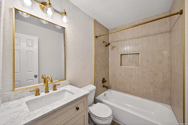 a bathroom with a granite countertop bathtub shower sink mirror vanity and toilet