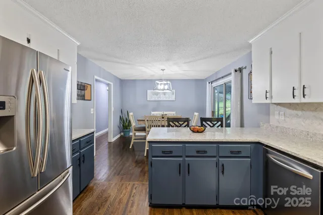 a kitchen with stainless steel appliances granite countertop a refrigerator a sink dishwasher a stove and white countertops with wooden floor