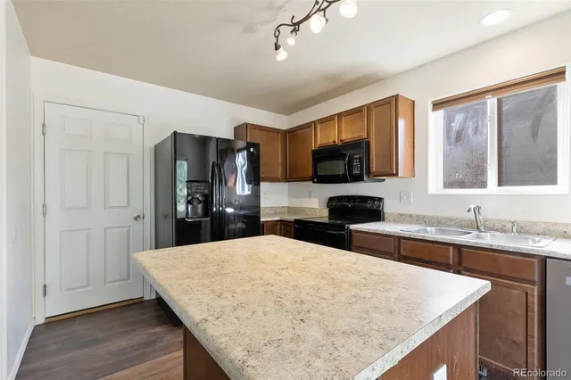 a kitchen with stainless steel appliances kitchen island granite countertop a refrigerator oven a sink dishwasher and wooden cabinets with wooden floor