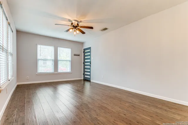 an empty room with wooden floor fan and windows